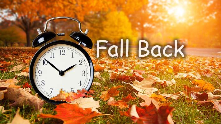 Alarm clock on the ground with leaves around it and the text Fall Back