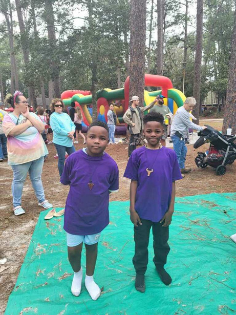 Two boys standing on a tarp in front of a bounce house smiling for a picture.