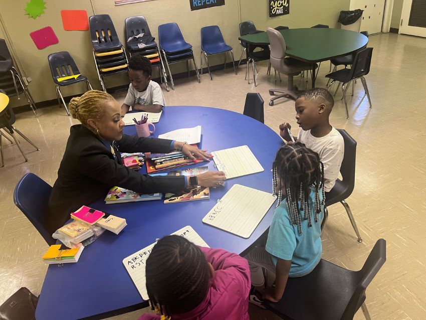 A woman helping children write their ABCs on a white board.