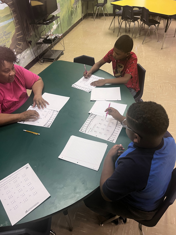 Two boys working on a math worksheet with a teacher.