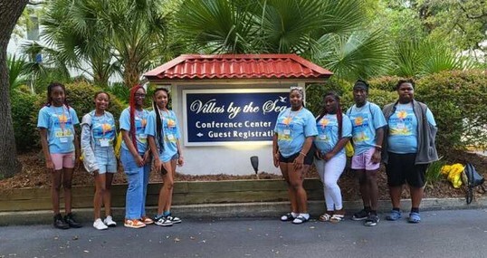 Young women standing outside of the Village by the Sea sign.