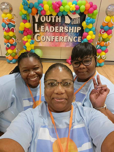 Three women standing next to a sign reading, Youth Leadership Conference.