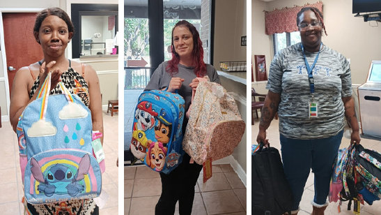 Residents standing and holding up backpacks while smiling.