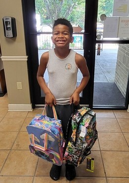 Young person holding backpacks and smiling. 