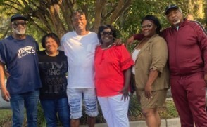 A group of people standing outside in front of a tree.