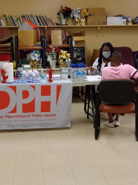 A resident sits at a table with a woman who is wearing a mask.